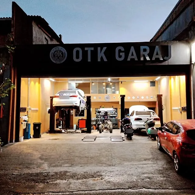 OTK Garaj atölyesinin akşam görünümü: tabela, liftteki araç ve içerideki motosikletler